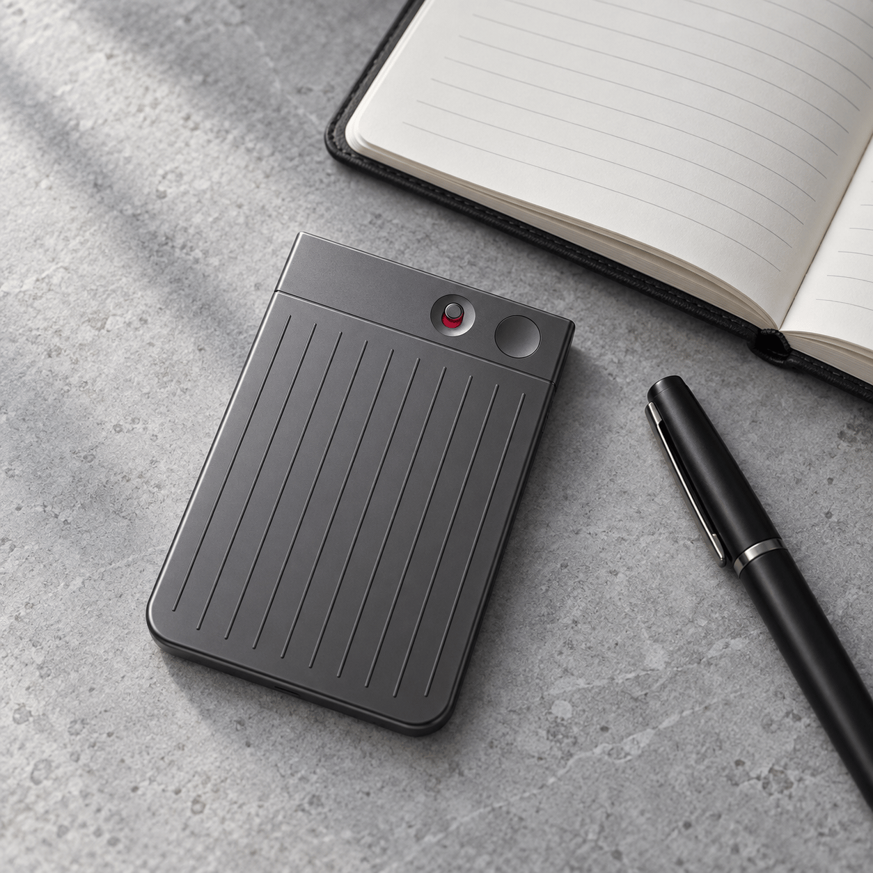 PLAUD Note recorder beside a notebook and pen.